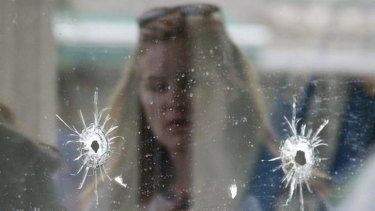 A woman looks at the bullet holes on the window of IV Deli Mark where Friday night's mass shooting took place.