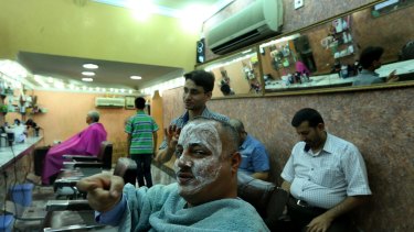 Brave face: Asaad Matoori makes the sign for a trigger while discussing Islamic State at a barber's shop in Baghdad.