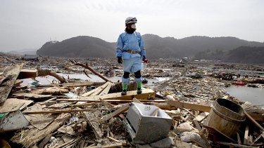 A rescue worker stands atop rubble during a body recovery mission in Ofunato.