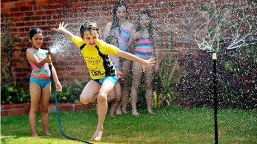 A backyard sprinkler and hose are put to traditional summer use. Sprinklers are permitted between 6pm and 10am.