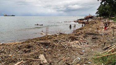 Locals walk amongst debris that was washed ashore near Honiara.