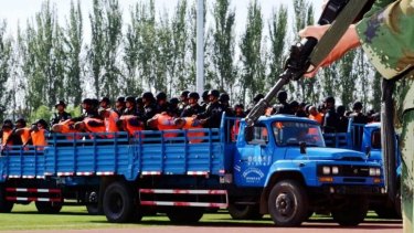 Accused men wearing orange vests are brough to a venue in Yili prefecture, Xinjiang, for mass sentencing on Tuesday.