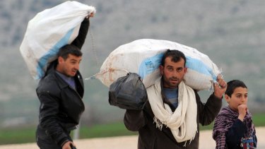 Syrian refugees carrying bags arrive near the border between Syria and Turkey at Reyhanli in Antakya