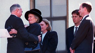 Then prime minister John Howard hugs then senator Jocelyn Newman at the funeral for her husband Kevin, while Campbell Newman (far right) looks on.