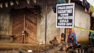 A chid stands near a sign advising of a quarantined home in Sierra Leone.
