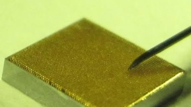A 4mm square gold-coated microneedle array next to a 31-gauge needle used to extract fluid.