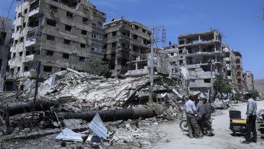 People stand in front of damaged buildings, in the town of Douma, the site of a suspected chemical weapons attack, near Damascus, Syria.