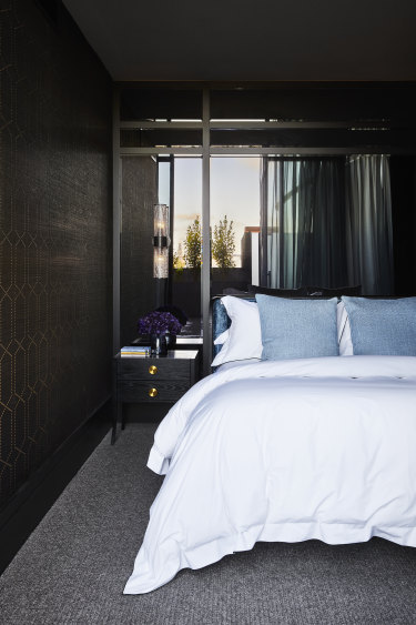A bedhead upholstered in a deep blue velvet from Gorsia is placed against a mirror-panelled wall that reflects the sky. The bedside table is from James Said.