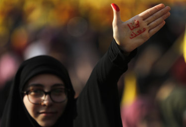 A Hezbollah supporter waves her hand with Arabic reading: "With you".