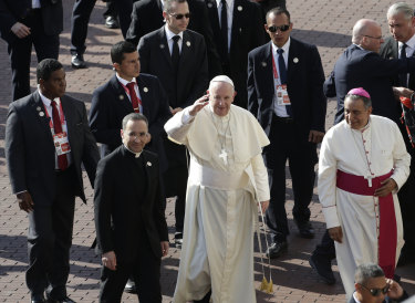 Flanked by a security detail, Pope Francis waves to the crowd.