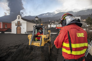 La policía militar retira la ceniza negra de un volcán que entra en erupción detrás de una iglesia en las Islas Canarias en La Palma, España.