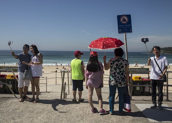 Tourists on Bondi Beach taking selfies with selfie sticks.