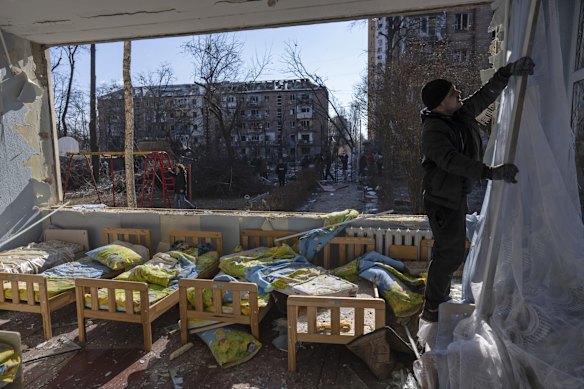 A man removes a destroyed curtain inside a school damaged among other residential buildings in Kyiv.