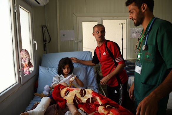 Mohamad Hazim, centre, and nurse Alaa Suliaman, right, talk with Mohamad's daughter Taiba, 7, who suffered bone deep shrapnel wounds and a broken leg. Five members of their family are still missing.