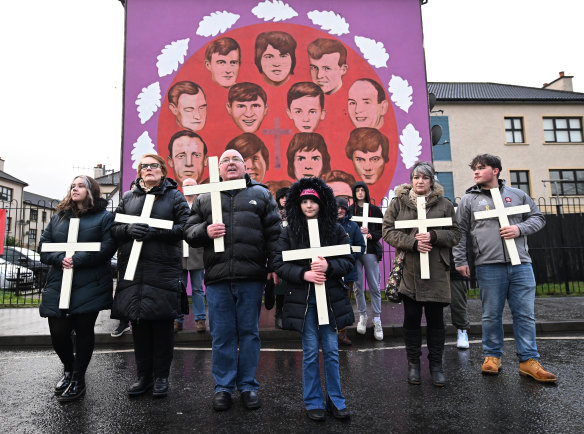 Families of the victims and supporters holding crosses walk past a mural featuring the 14 victims as they take part in the 50th anniversary Bloody Sunday March to Free Derry Corne Londonderry, Northern Ireland.