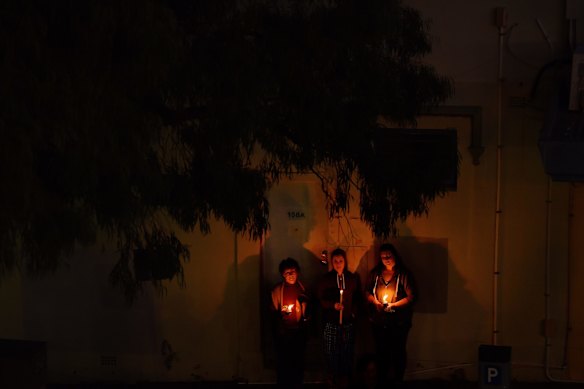 Three women holding candles listen to bugler Sarah Brown as she plays The Last Post from the balcony of The Royal Hotel in Leichhardt at dawn on ANZAC Day. 