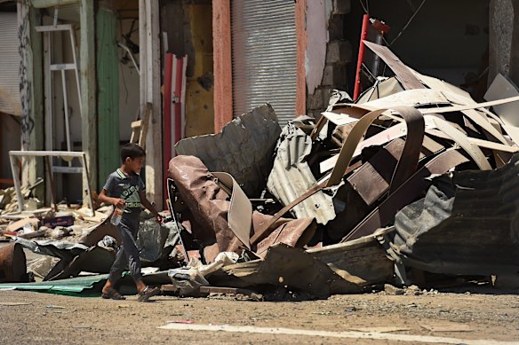 A boy walks across a street surrounded by debris and destroyed buildings.