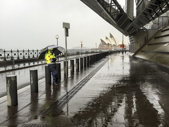 A security guard endures the rain under The Sydney Harbour Bridge.