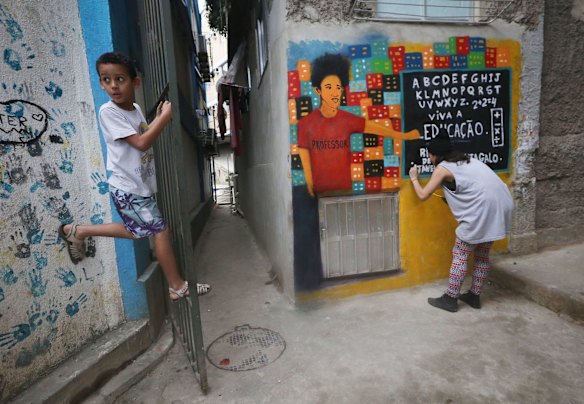A young resident hangs on a grate (L) as artist Flora Prospero paints street art along the alleyway leading to the Tiki Hostel in the Cantagalo favela.
