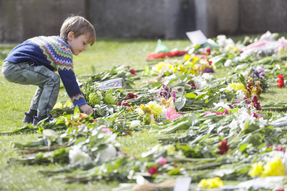 A child lays flowers outside the Cambridge gate of Windsor Castle in Windsor, England after the announcement about the death of Britain’s Prince Philip.