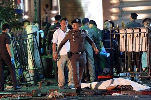 A police officer walks by the body of a victim covered in a white sheet following an explosion at the Ratchaprasong intersection in Bangkok.