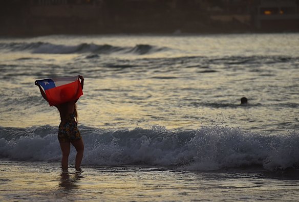 A woman holds the Chile flag as the sun rises over Bondi Beach, Sydney. Hundreds of people gathered on Bondi Beach to bring in the new year. 