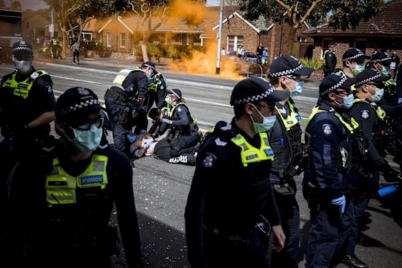 A man is taken to the ground by police as a flare goes off in the background at Melbourne’s anti-lockdown rally.