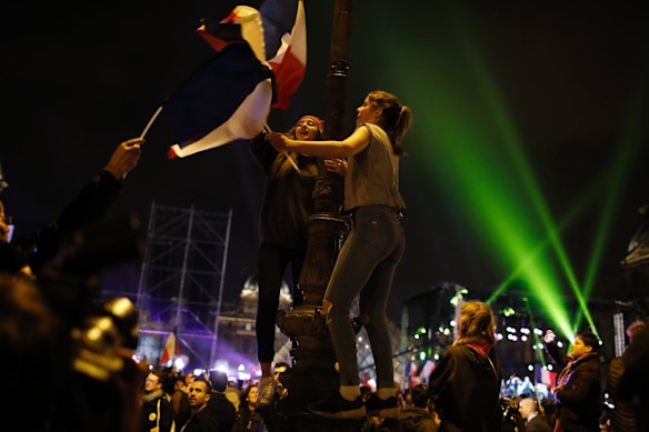 Women dance with French flags on a street lamp with a French flag at the Louvre museum where Emmanuel Macron celebrated his victory, Sunday, May 7, 2017 in Paris.