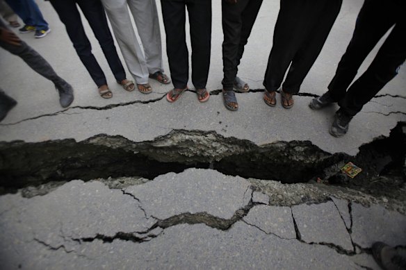 Nepalese people look at a cracked road after an earthquake in Kathmandu, Nepal, Sunday, April 26, 2015. 