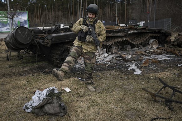 A Ukrainian serviceman kicks a burnt sleeping bag near the wreck of a Russian tank in Stoyanka, Ukraine.