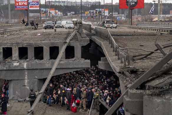 Ukrainians crowd under a destroyed bridge as they try to flee across the Irpin River in the outskirts of Kyiv, Ukraine.