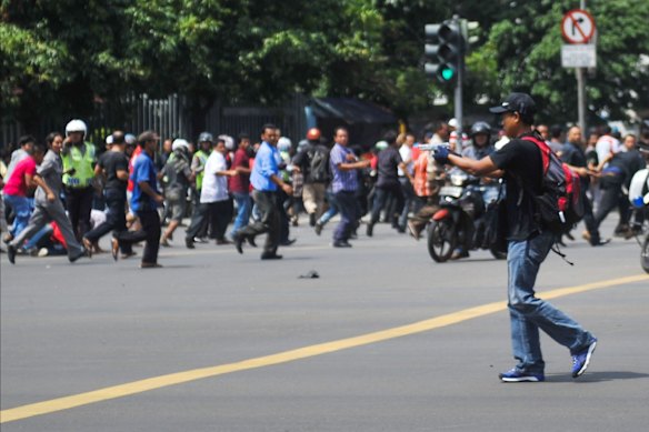 In this photo released by China's Xinhua News Agency, an unidentified man with a gun walks in the street as people run in the background on Thamrin street near Sarinah shopping mall in Jakarta, Indonesia, Thursday, Jan. 14, 2016