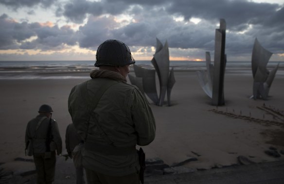 Two men in vintage US WWII uniforms walk toward the Les Braves monument at sunrise prior to a D-Day 76th anniversary ceremony in Saint Laurent sur Mer, Normandy, France, Saturday, June 6, 2020. 