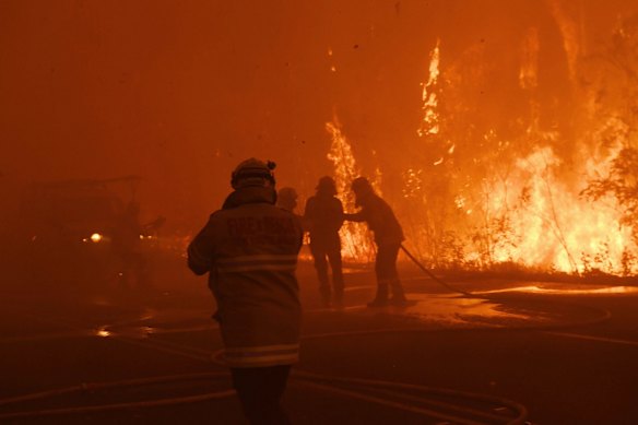 Firefighter from fbnsw stumbles after being hit in smoke and helped back to safety as Gospers mt fire crosses bells line. Late on December 21, 2019. 