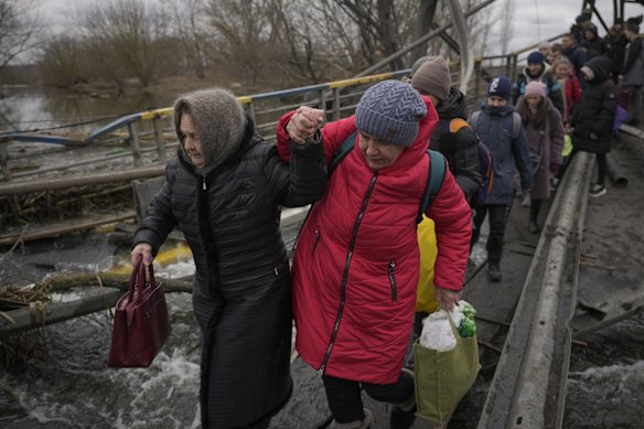 Women hold hands while crossing the Irpin river on an improvised path under a bridge that was destroyed by a Russian airstrike, while assisting people fleeing the town of Irpin, Ukraine.