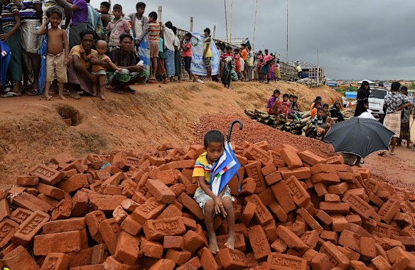 A young Rohingya boy sits on a pile of bricks holding his umbrella after a monsoonal rain in Hakim Para Camp.