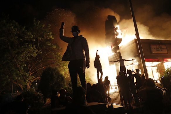 Protesters gather in front of a burning fast food restaurant.
