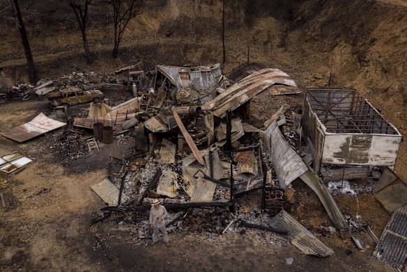 Mark Brooks, 60, is dwarfed (at front of frame) by the wreckage of his burnt out home in Upper Thowgla valley near Corryong.