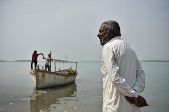 Budha Ismail (right) watches his fishing boat and crew land on the beach near the Tragadi Bandar fishing settlement, which has been heavily impacted by the Adani Group's nearby port and power plant. "We used to go two kilometres out to sea to get the fish – now we have to go 10," he says.