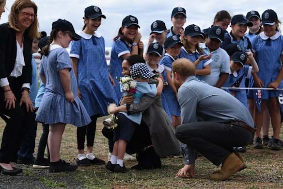 Prince Harry, the Duke of Sussex looks on as his wife Meghan, the Duchess of Sussex is hugged by a student Luke Vincent of Buninyong Public School following their arrival at Dubbo Regional Airport.