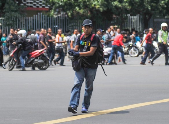 In this photo released by China's Xinhua News Agency, an unidentified man with a gun walks in the street as people run in the background on Thamrin street near Sarinah shopping mall in Jakarta, Indonesia, Thursday, Jan. 14, 2016. 