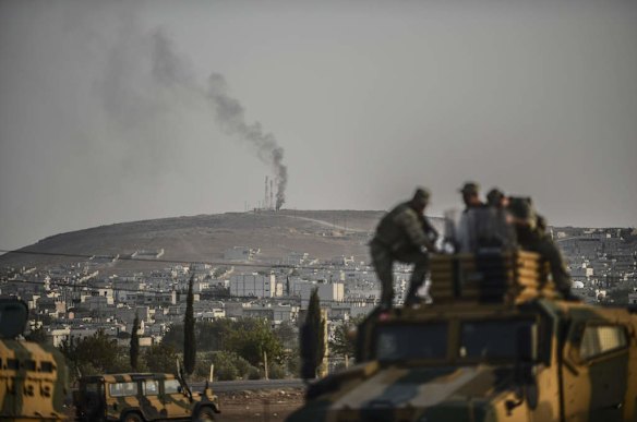 Smoke rises from the Syrian town of Ain al-Arab, known as Kobane by the Kurds, as Turkish soldiers take position in the southeastern town of Suruc, Sanliurfa province, near the Mursitpinar border crossing with Syria on October 3, 2014.  Photo by AFP