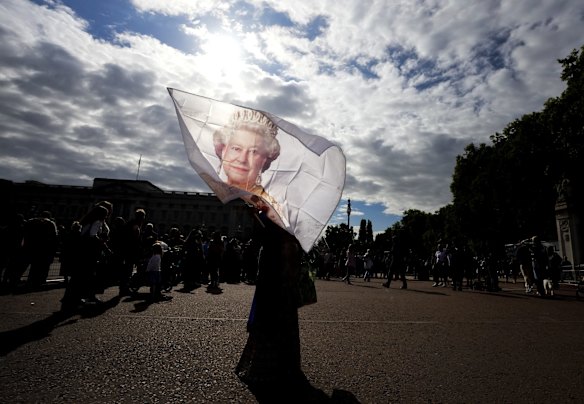 A flag is waved with an image of the late Queen Elizabeth II as thousands of people mourn and pay their respects at the gates of Buckingham Palace in London, United Kingdom