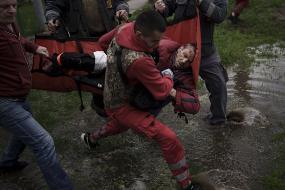 An emergency worker is helped by locals to carry a man to an ambulance following a Russian bombardment in Kharkiv.