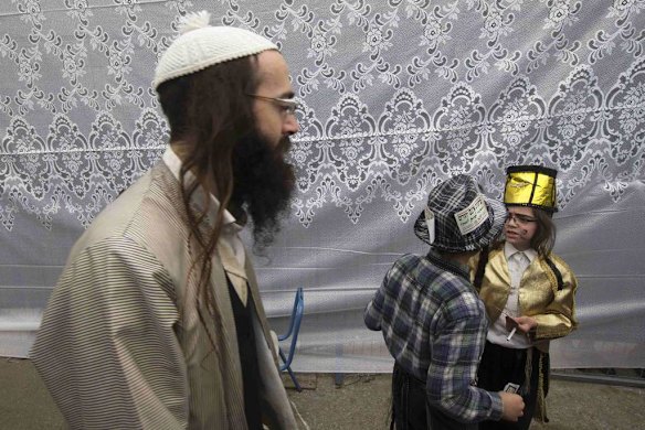 An ultra-Orthodox Jewish man walks past children wearing costumes.