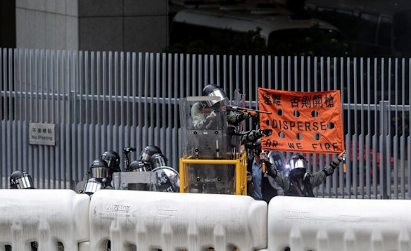 Riot police point a non-lethal weapon toward demonstrators while raising a banner reading 'Disperse Or We Fire' outside the Central Government Offices during a protest in the Admiralty district.
