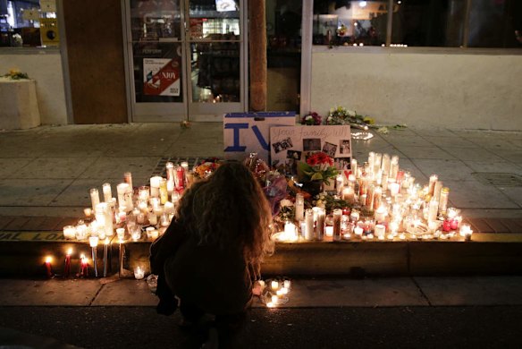 A woman places a candle in front of IV Deli Mart, where par of Friday night's mass shooting took place by a drive-by shooter.