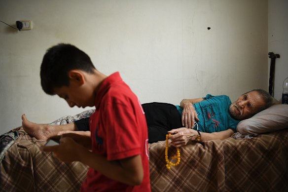 Syrian refugees Mohammad al-Deraai, 13 (left) looks at a mobile phone watched by his ill uncle Sobhi al-Deraai (right) in the family apartment in Ain al-Hilweh a Palestinian refugee camp in Sidon, Lebanon. The family have been refused UNHCR assistance so Mohammad is supporting the family by selling soaps and socks on the street in Ain al-Hilweh camp.