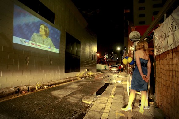Supporters of LNP candidate for South Brisbane, Fiona Ward, watch  election coverage projected onto a laneway wall.