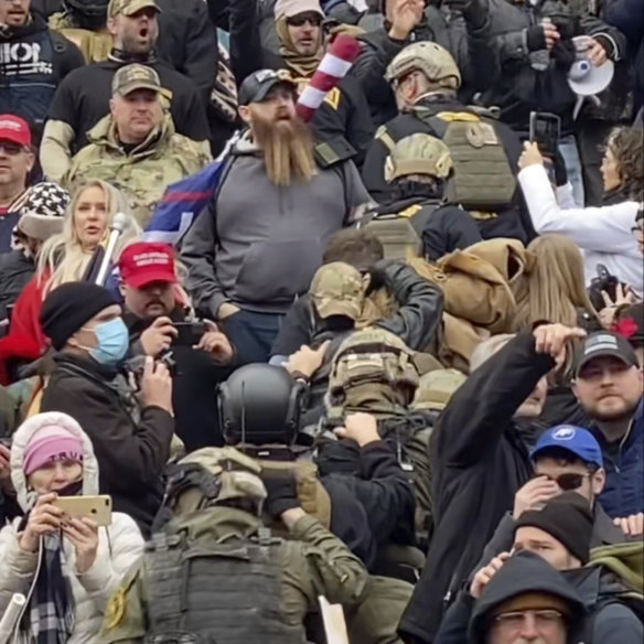 A line of men wearing helmets and body armour walk up the stairs outside the US Capitol on January 6 in single file, each man holding the jacket collar of the man ahead.